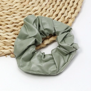 Detailed view of a sage green PU leather scrunchie with soft texture on a woven mat