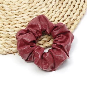Close-up of wine red faux leather hair scrunchie with soft pleated texture on woven mat