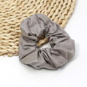 Detailed view of the soft grey faux leather scrunchie with elegant pleated texture