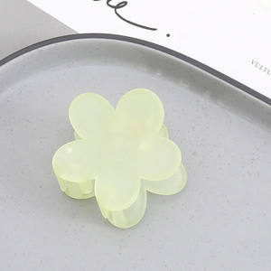 Close-up of a light green matte flower hair claw clip on a gray textured plate
