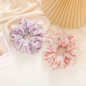 Floral print hair scrunchies in pink and purple colors on a textured cream fabric