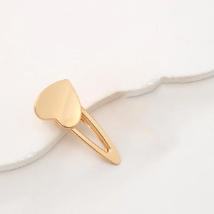 Barrette à cheveux dorée en forme de cœur sur un support en pierre minimaliste