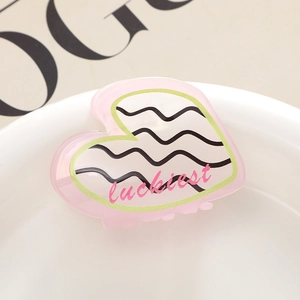 Vue macro de la pince à cheveux cœur rose avec texte luckiest et détails ondulés sur porcelaine