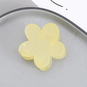 Detail view of a matte yellow flower hair claw clip on a minimalist ceramic plate