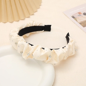 Détail d'un serre-tête en satin plissé crème orné de strass sur un fond texturé élégant