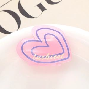 Détail de la pince à cheveux cœur rose avec bordure violette et texte luckiest gravé