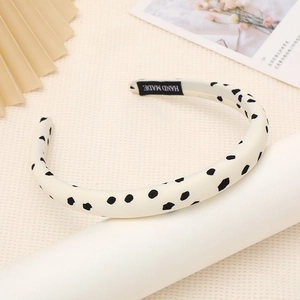 Detailed close-up of a wide sponge headband featuring black polka dots and a handmade label