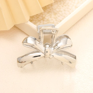 Elegant silver metal bow hair claw clip for women on a minimalist textured background