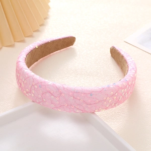 Détail du serre-tête rose à paillettes avec dentelle et rembourrage sur fond beige