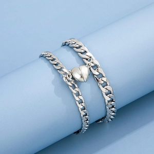 Detail of two silver curb chain bracelets with magnetic heart pendants on blue stands