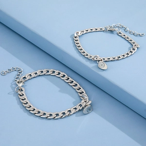 Detail of silver curb chain bracelets with magnetic heart clasps on a modern blue background