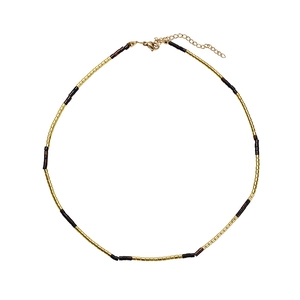 Detail van minimalistische kralenketting met gouden en donkere cilinderkralen en karabijnslot