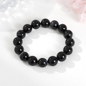 Natural black obsidian beaded bracelet for men and women on a stylish white textured surface