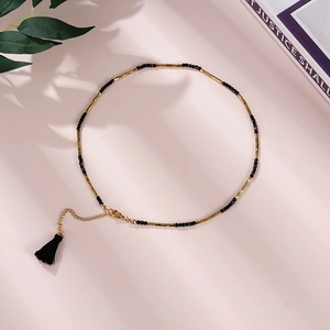 Detail of beaded necklace with gold tubes, black beads, and silk tassel on pink background