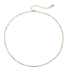 Detail of beaded necklace featuring green stones, gold accents, and a blue tassel charm