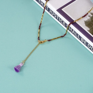 Detail of beaded necklace with gold tubes, dark red beads and purple tassel accent