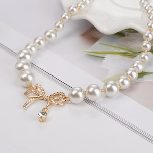 Gros plan d'un collier de perles avec un pendentif nœud doré et une goutte de diamant
