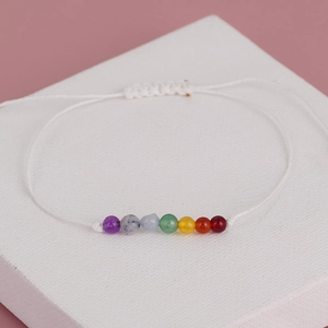 Macro shot of handmade white woven cord bracelet with seven colorful chakra gemstone beads