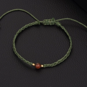 Adjustable woven turquoise bracelet with red agate bead on black leather background