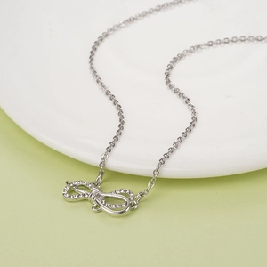 Silver bow necklace with crystal tassels and polished chain on white ceramic plate