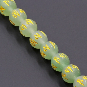 Macro detail of natural light green crystal beads with golden mantra engraving and smooth texture