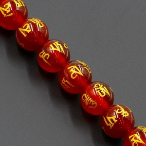 Macro detail of red translucent crystal beads with gold Mantra character engravings