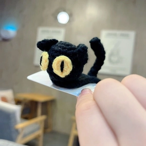 Handmade knitted black cat headband with yellow eyes on a white display card