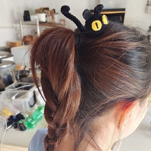 Detail of a handmade black knitted cat hair tie showing woven texture and yellow eyes