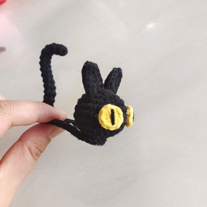 Detailed close-up of hand-knitted black cat headband with yellow eyes in hand