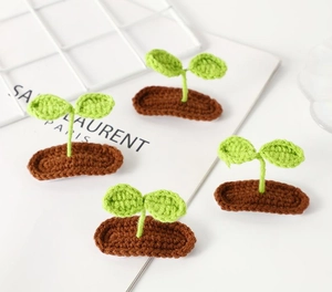 Detail view of four handmade crochet sprout hair clips with green leaves and brown soil base