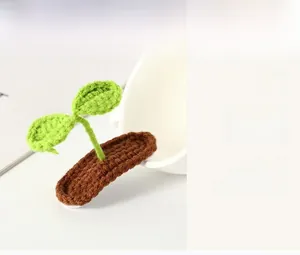 Detailed close-up of a handmade knitted green sprout hair clip on a white ceramic cup