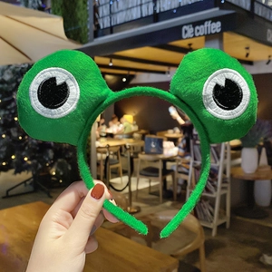 Close-up of green plush frog headband with detailed black and white eye embroidery