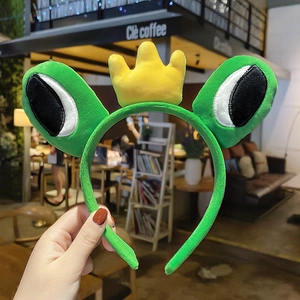 Close-up of a green plush frog headband featuring a cute yellow crown and big eyes