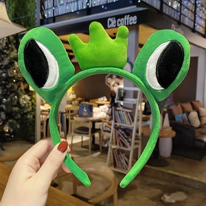 Close-up of cute plush green frog headband with cartoon eyes and small crown