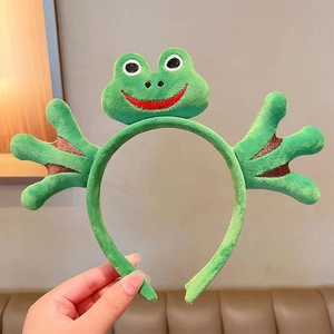 Detail view of plush green frog headband featuring embroidered eyes and cute webbed feet