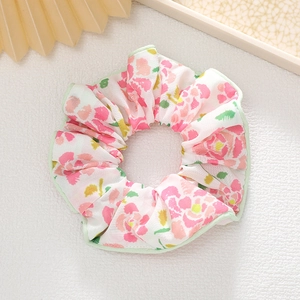 Détail d'un chouchou à imprimé fleuri avec fleurs roses et bordure de passepoil vert