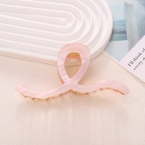 Elegant pink marble acetate shark hair claw with gold metal teeth in a minimalist setting