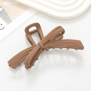 Pince à cheveux mate marron en forme de nœud avec design croisé sur fond minimaliste