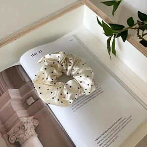 Chouchou en soie beige à pois noirs posé sur une revue ouverte au style minimaliste