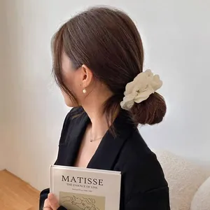 Nahaufnahme von cremefarbenem Chiffon-Haargummi und Perlenohrringen im Retro-Stil