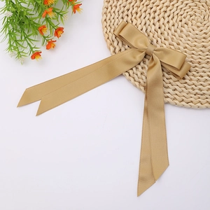 Detailed view of champagne satin double bow hair clip with long ribbons on woven mat