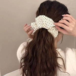 Polka dot fabric scrunchie in cream and black, shown worn on a ponytail for hair styling