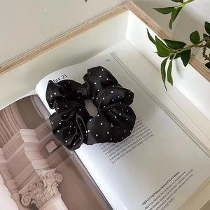 Détail d'un chouchou en satin noir à pois posé sur un magazine pour coiffure chic
