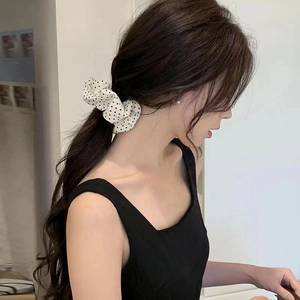Close-up of a white polka dot fabric scrunchie styled on a low ponytail hairstyle