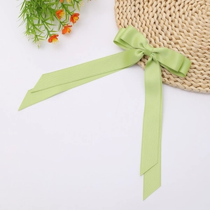 Close-up of a light green satin bow hair clip with long ribbons on a white background
