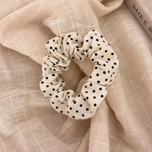 Close-up of cream polka dot fabric scrunchie on textured linen background with soft lighting