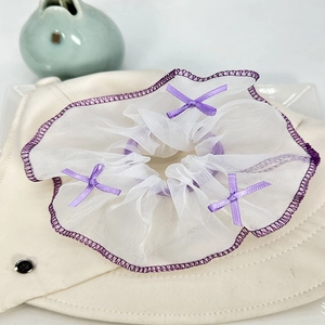 Gros plan d'un chouchou en tulle blanc avec nœuds violets sur un chapeau beige