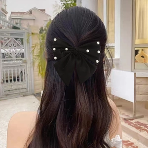 Detail view of a black satin bow hair clip with pearls on a half-up hairstyle