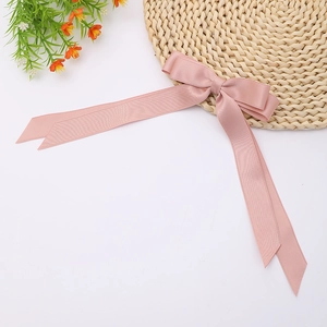 Detailed view of pink satin long tail bow hair clip on a woven mat with orange flowers