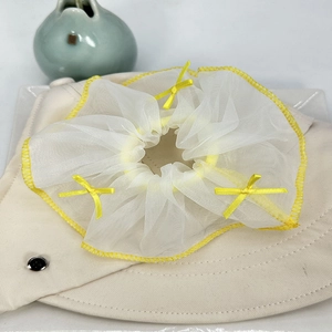 Détail d'un chouchou en résille blanche avec bordure jaune et petits nœuds jaunes